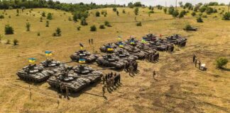 Rows of military tanks with soldiers assembled on a dry field