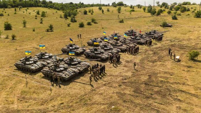 Rows of military tanks with soldiers assembled on a dry field