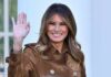 Melania Trump waving and smiling in a brown suede coat