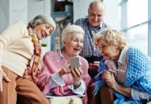 Later Retirement Wave Hits Hard Group of seniors smiling and looking at a smartphone together