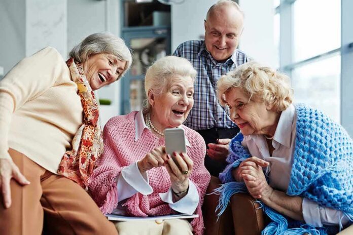shutterstock_615337679 Group of seniors smiling and looking at a smartphone together
