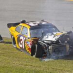 Racing Icon’s Mystery Brain Battle Race car with heavy front-end damage on grass