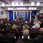 Trump’s Media Ban Turns Physical Press secretary at podium addressing reporters in briefing room