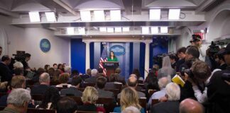 Press secretary at podium addressing reporters in briefing room