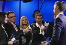 Access War Erupts – 14 Days Ticking Journalists interview a man in a suit with microphones