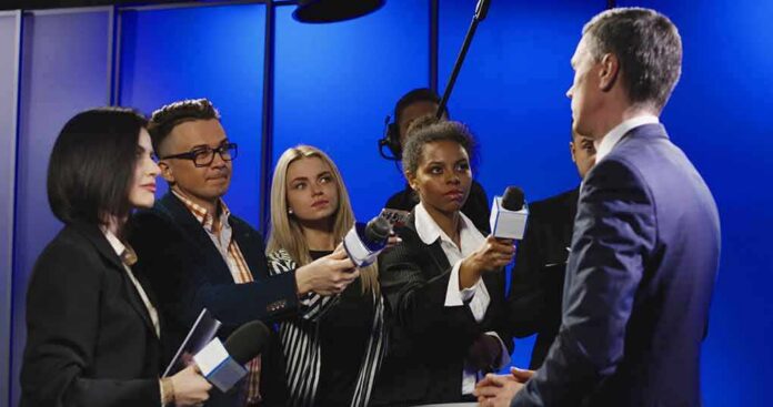 shutterstock_1030299358 Journalists interview a man in a suit with microphones