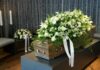 Whistleblower Found Hanged – Family Insists Suicide Coffin with white flower spray in a funeral setting