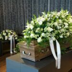 Whistleblower Found Hanged – Family Insists Suicide Coffin with white flower spray in a funeral setting