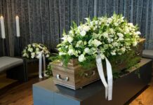 Whistleblower Found Hanged – Family Insists Suicide Coffin with white flower spray in a funeral setting