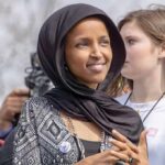 Feds Probe Rep. Ilhan Omar – What’s Hidden? Ilhan Omar wearing a black headscarf at an outdoor event