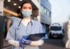 Plague Lab Panic Deepens – Records Missing? Healthcare worker in scrubs wearing mask and gloves holding a clipboard