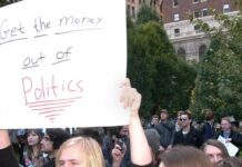Protesters holding a large handwritten sign at a crowded outdoor rally