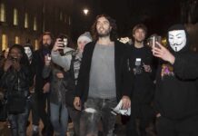 Prosecutors Paint Russell Brand as Serial Predator Russell Brand walking with a crowd at night