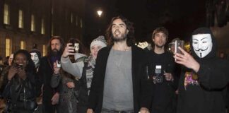 Russell Brand walking with a crowd at night