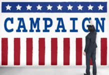 Proof-Of-Life Demands Rock Talarico Race Man in suit writing on large campaign banner with stars and stripes